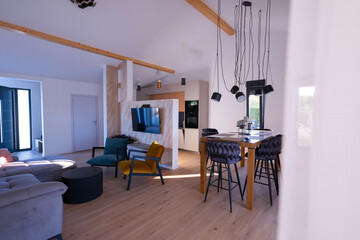 Modern open-plan living and dining area with an integrated kitchen, featuring a comfortable sofa, stylish armchairs, and a bar-height dining table. Wooden floors and ceiling beams enhance this