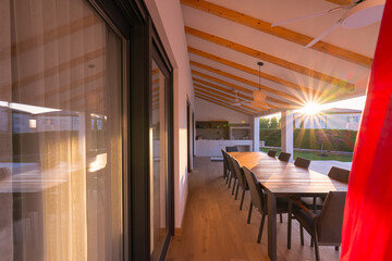 Modern villa with a stunning swimming pool and spacious wooden deck, perfect for outdoor dining. Capturing the golden hour with a beautiful sunset and clear sky, showcasing luxury living and serene