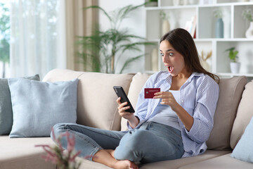 Surprised woman in blue buying online in a house interior
