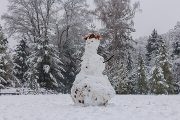 Real imperfect snowman in snowy winter forest during snowfall