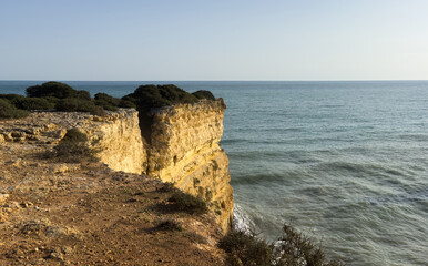 Waves crashing against the rocky coastline near Praia da Morena, Algarve, Portugal, seascape under a clear blue sky