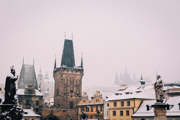 Obraz premium A breathtaking view of Prague's iconic towers and rooftops blanketed in snow, creating a serene winter scene.