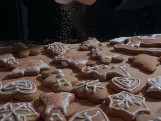 Gingerbread cookies on a wooden board with a hand sprinkling sparkling sugar over them against a dark background.