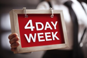 man employee holding a sign with writing 4 day week standing in office