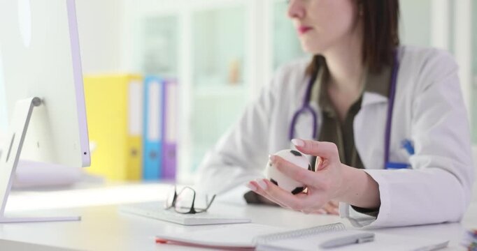 Doctor studies information on computer and squeezes anti-stress toy to relieve tension. Woman focuses on patient information displayed on monitor