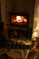 Young woman relaxing by the fireplace in a cozy house on a winter evening