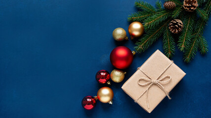 Festive Christmas ornaments and gift box on a deep blue background, top view, text space