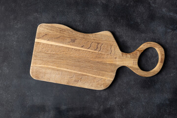 Old wooden cutting board on a black slate background, top view copy space