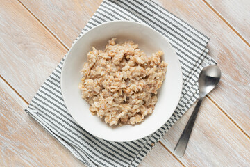 Healthy vegan breakfast meal: cooked oatmeal and spelt porridge in white bowl served with cup of coffee and almond milk in jug