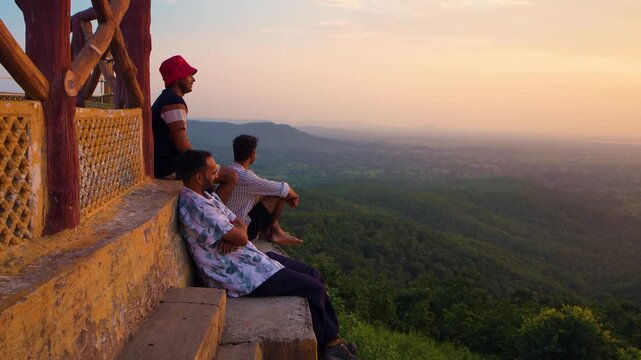 Three hikers trekking during sunset in the mountains under a partly cloudy sky, with a temple creating a breathtaking backdrop at Samai Mata Mandir, Banswara, near Udaipur, Rajasthan, India.