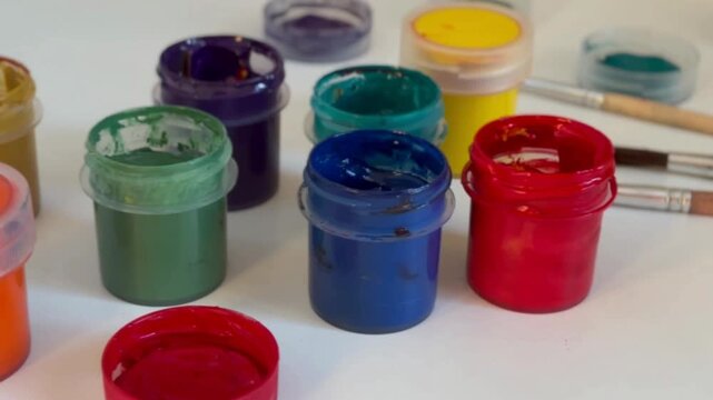 A set of gouache paints in jars, vibrant colors, close-up. Brushes and paints on a table. Art, hobby, school