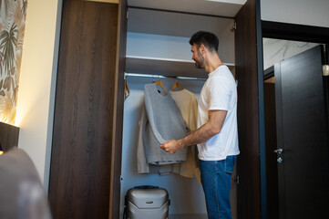 Dark-haired caucasian man checking his clothes in a wardrobe in a hotel