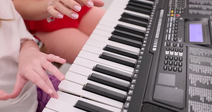 Woman encourages child to repeat short musical phrase on synthesizer. Daughter experiments with different sound settings on synthesizer. Slow motion