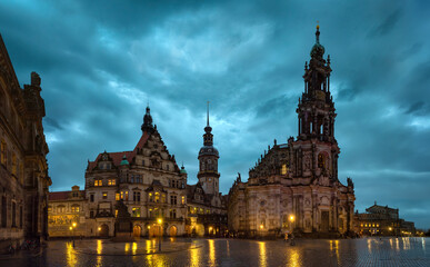 Evening view of Dresden Cathedral and historic buildings at Theater Square with illuminated baroque architecture, dramatic cloudy sky, and wet reflections in the old town of Saxony, Germany
