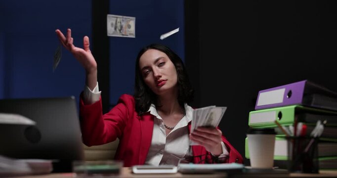 Tired office worker in red blazer waves banknotes at desk. Woman counts cash for salary throwing bills in air while feeling exhausted slow motion