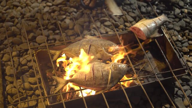 Delicious sea bream fish grilling on a barbecue, seasoned with lemon slices, emitting smoke and aroma.
