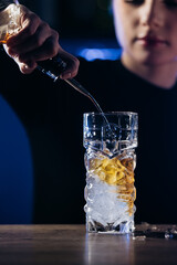 Bartender pouring a drink into a glass filled with ice, showcasing cocktail preparation skills in a vibrant bar environment with atmospheric lighting and modern decor
