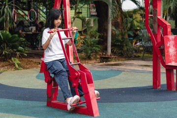 An Indonesian little girl trying an outdoor gym equipment. Iron exercise bike in a park.