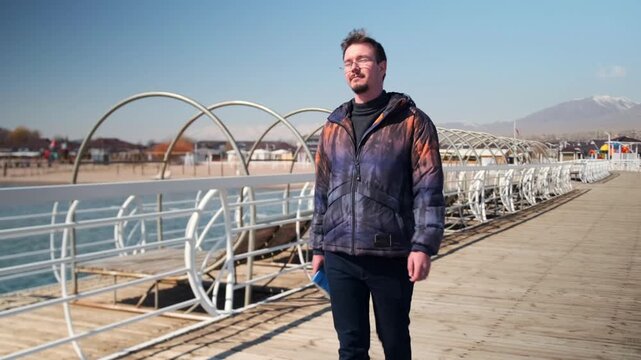 author near water, scribe strolls by oceanfront, writer wanders along seaside, novelist takes walk beside glittering water, an author leisurely walks along beautiful and serene waterfront area