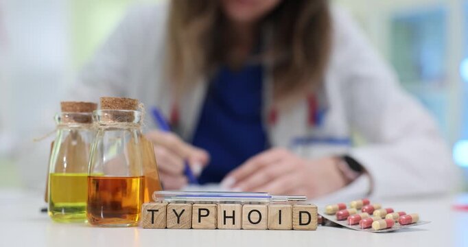 Wooden cubes on medical desk spell Typhoid creating focus on infectious disease. Female doctor in coat writes notes in modern clinic with bottles