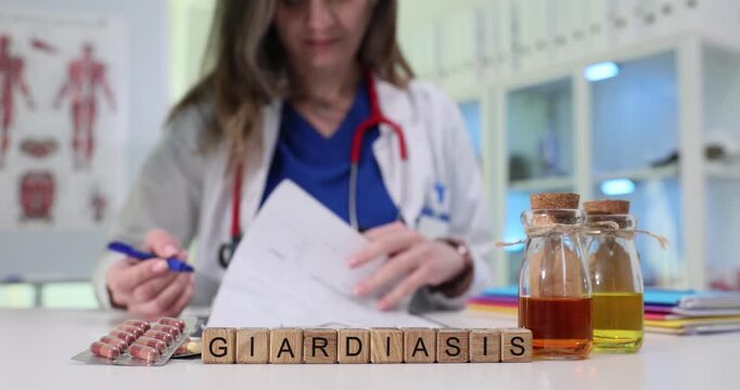 Wooden blocks form word Giardiasis on desk with medicine bottles and blister pack. Female doctor in scrubs checks test results in clinical laboratory