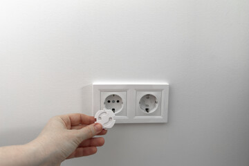 Hand holding child safety plug for electrical outlet installation, demonstrating proper usage of electrical components in a modern home environment with minimalistic design