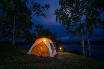 Night camping adventure with a cozy tent lit under the starry sky in a summer forest
