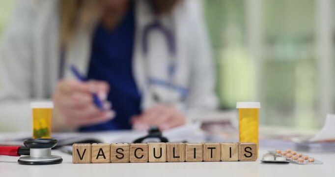 Wooden cubes spell word Vasculitis on desk with pill bottle and stethoscope. Female doctor writes notes about diseased vessels in modern clinic