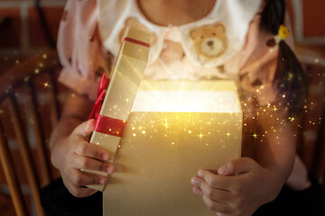 Close-up of Child's Hands Opening Magical Gift Box with Sparkling Golden Light for Christmas Surprise