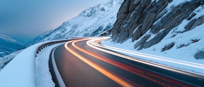 A long exposure shot of a mountain road with snow on the sides and light trails from passing vehicles