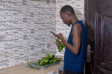 handsome man in her home kitchen, focused on the task of cutting fresh, green vegetable while using his phone