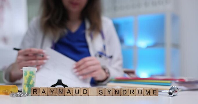 Woman doctor writes out clear and structured therapy schedule for patient. Medical term Raynaud Syndrome arranged on table with miniature wooden cubes