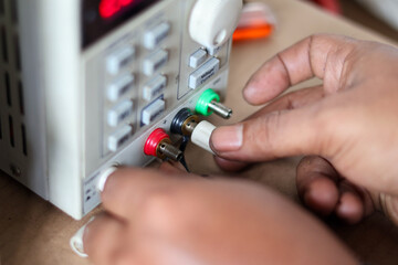 Hands connecting banana plugs to a laboratory DC power supply unit for testing and electronic troubleshooting.