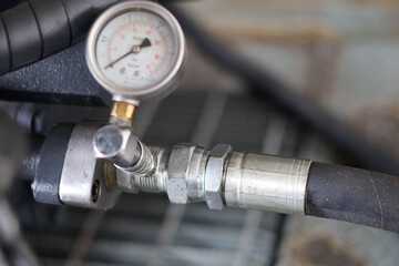 Close-up of a pressure gauge connected to a hydraulic hose or pipe assembly for measuring system pressure on industrial machinery.