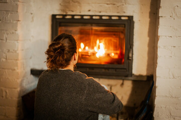 Young woman relaxing by the fireplace in a cozy house on a winter evening