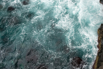 Obraz premium Overhead view of white sea foam swirling around dark rocks