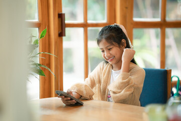 A young girl sits comfortably indoors,focused on her phone as warm light gently surrounds her.