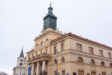 New City Hall in Lublin, Poland. A large building stands in the city center with a tall clock tower. Flags fly from the roof on a gray day in winter.