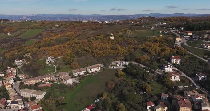 Aerial view of the landscape, showcasing houses nestled amongst golden trees and green fields under a clear blue sky, Gesualdo, Irpinia, Italy.