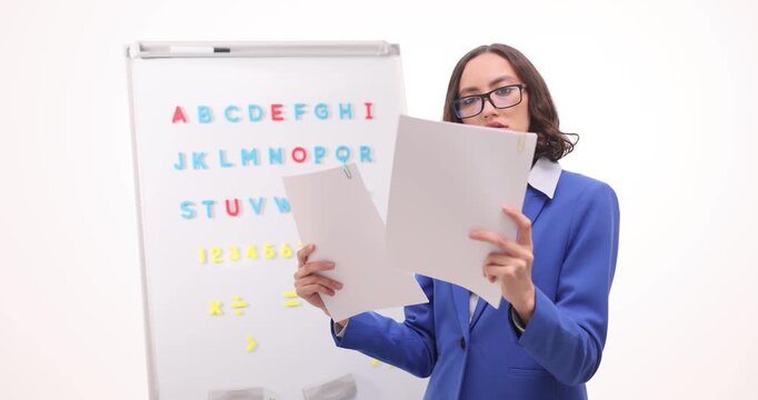 Woman teacher stands near whiteboard with colorful alphabet. Educator holds worksheets reading rules and showing disappointment moving shoulders