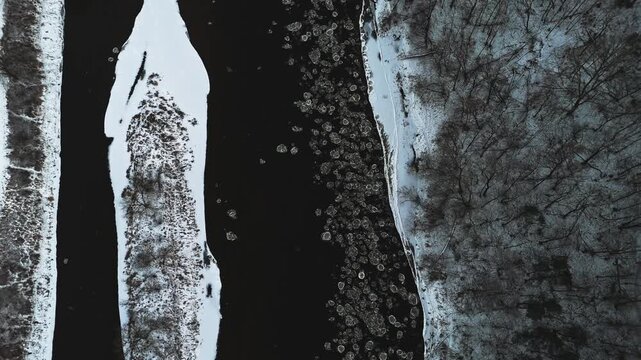 Aerial view of a river with chunks of ice floating in contrast to the snow covered forest creating stark contrast, Vilnius, Lithuania.