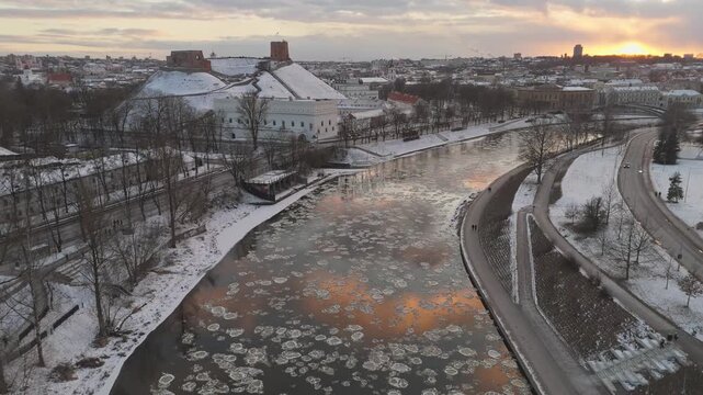 Aerial view of the snow-covered landscape, the river with ice floes reflects the warm sunset near Gediminas' Tower, Vilnius, Lithuania.