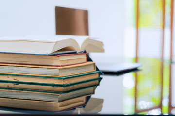 A stack of several books is placed on a table, with the top book left open
