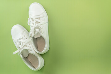 Still life of a pair of clean white sneakers and four rectangular white cleaning sponges against a solid light green background.