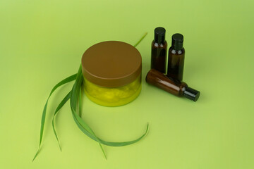 Still life of green cosmetics in a jar and three brown bottles, decorated with green stems on a lime background.