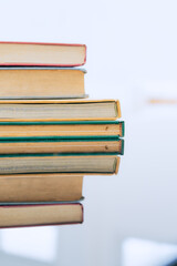A stack of several books is placed on a table, with the top book left open