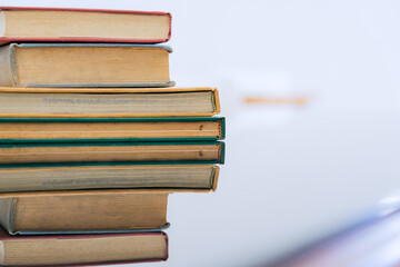 A stack of several books is placed on a table, with the top book left open