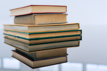 A stack of several books is placed on a table, with the top book left open