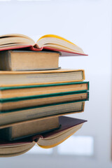 A stack of several books is placed on a table, with the top book left open