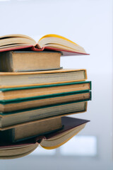 A stack of several books is placed on a table, with the top book left open